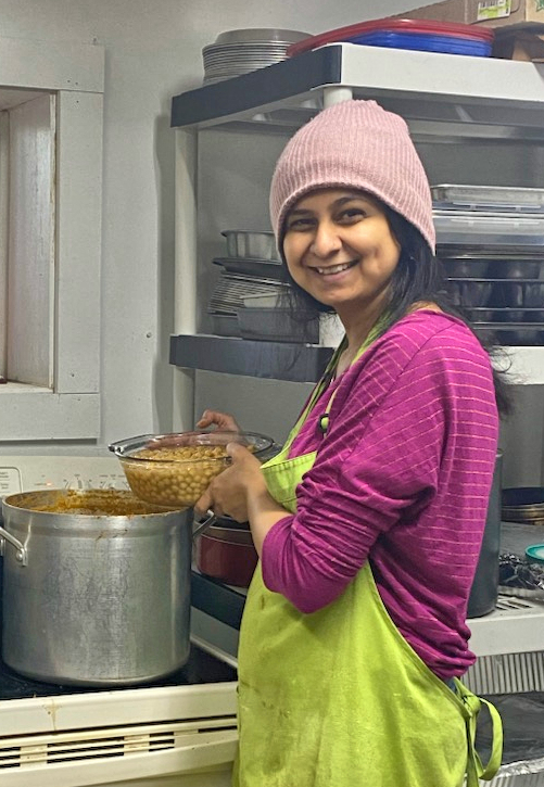 Big smile with colorful clothes and apron, holding bowl of beans near a big pot